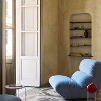 Blue lounge chair with soft curves, set against a warm beige wall and patterned mosaic floor. Minimalist decor accents.