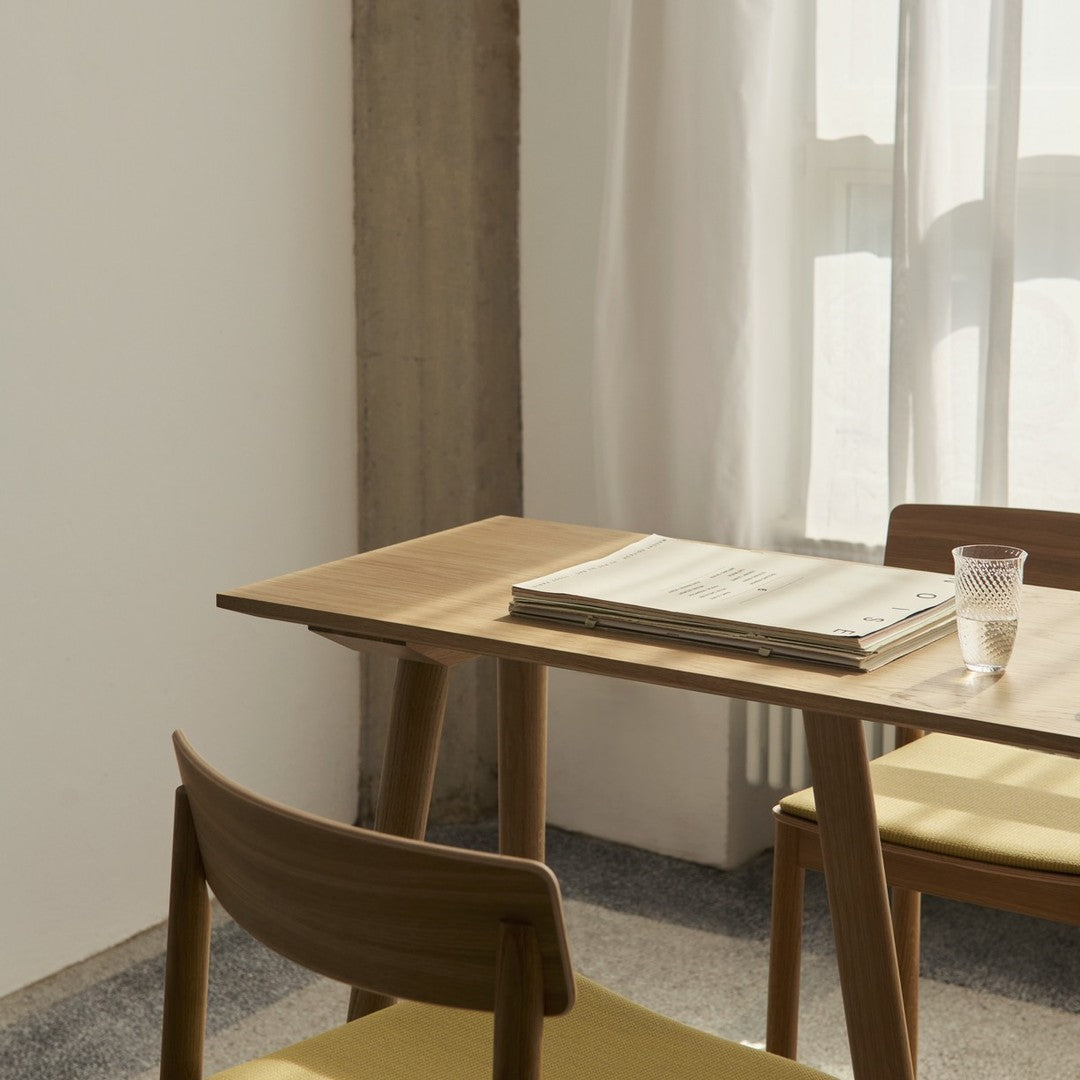 Modern wooden table with light beige chairs, complemented by soft natural light and a neutral background.