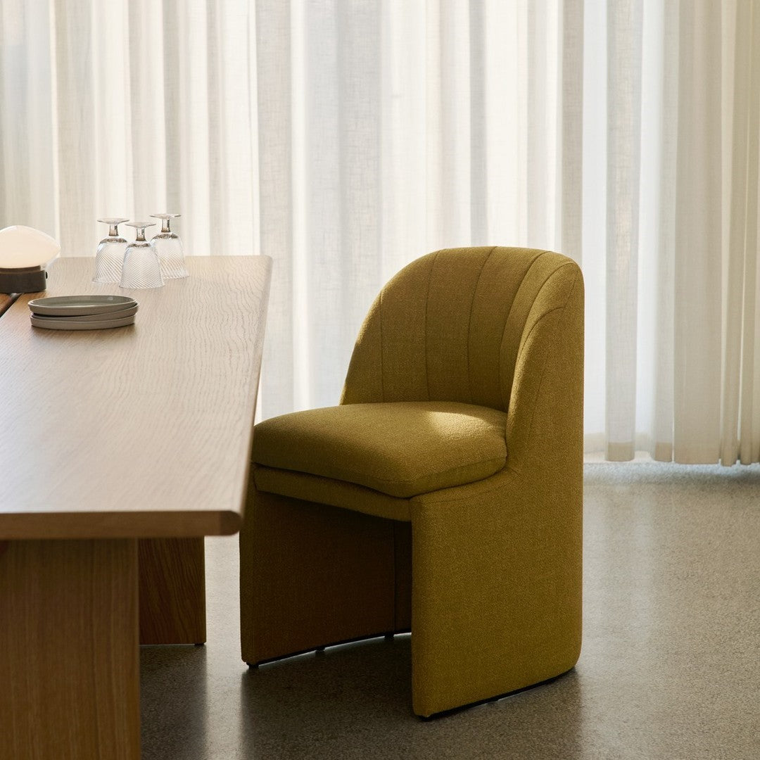  upholstered chair in mustard yellow with a ribbed pattern, set near a wooden table and light curtains.