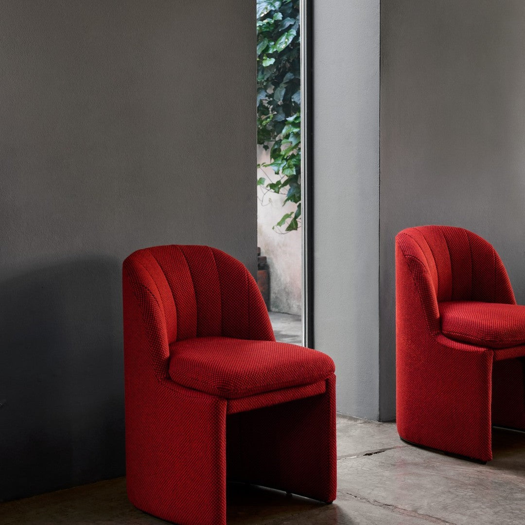 Red upholstered chairs with vertical ribbed pattern, set against a gray wall and natural greenery backdrop.
