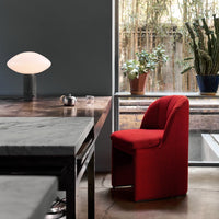 Red patterned chair on a wooden table with a marble surface, surrounded by green plants in a modern setting.