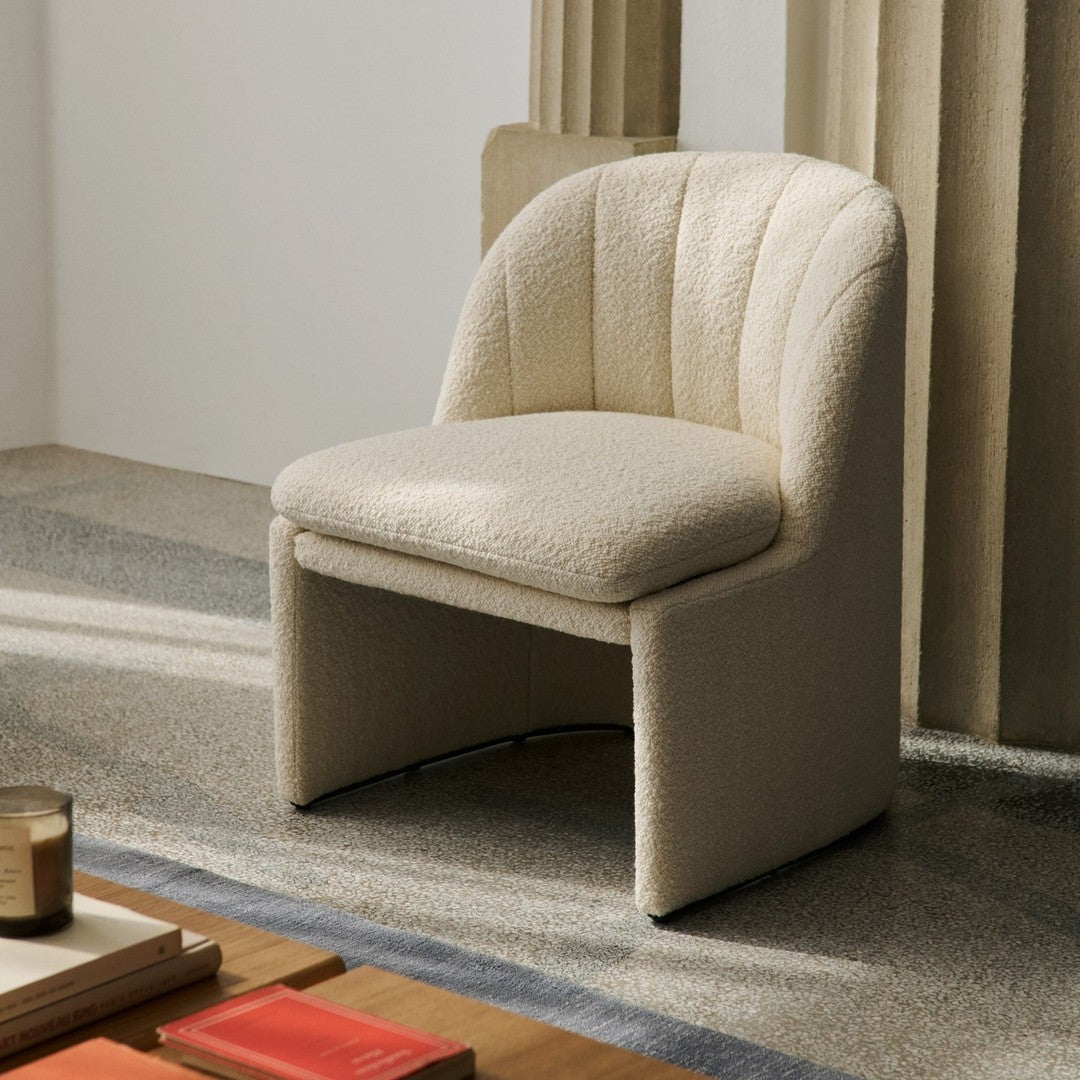 Cream-colored upholstered chair with a textured pattern and curved backrest, set against a neutral backdrop.