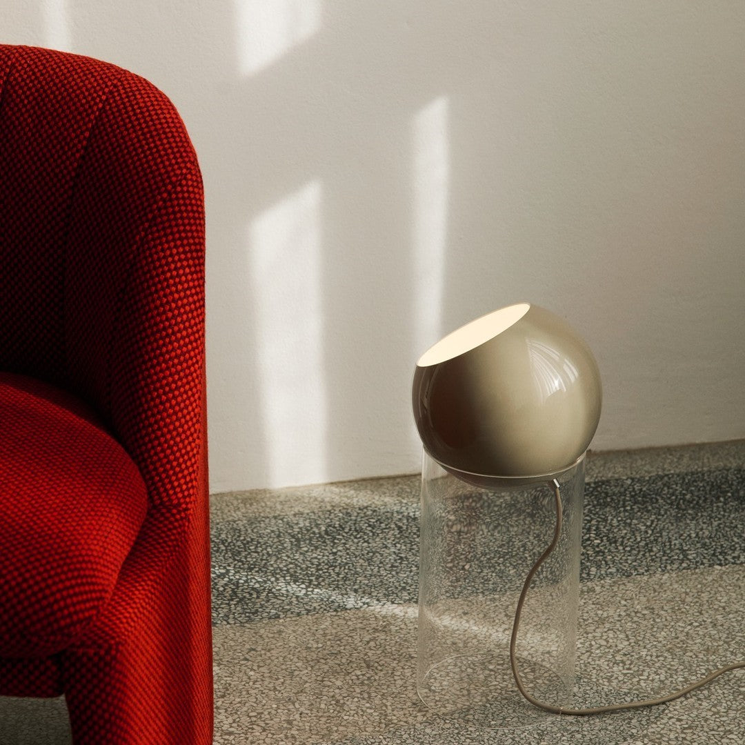 Red textured chair with a beige lamp on a clear base, set against a light background with subtle shadows.