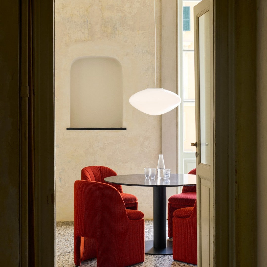 Red textured chairs surround a sleek black round table, complemented by a contemporary white pendant light.