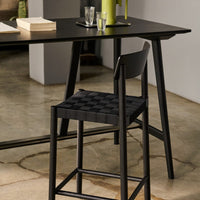 Black checkerboard-patterned seat on a modern black stool beside a sleek black table in a minimalist setting.