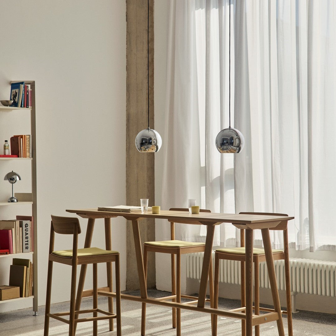 Modern dining area featuring brown wood, yellow cushions, and sleek chrome pendant lights against bright, airy curtains.