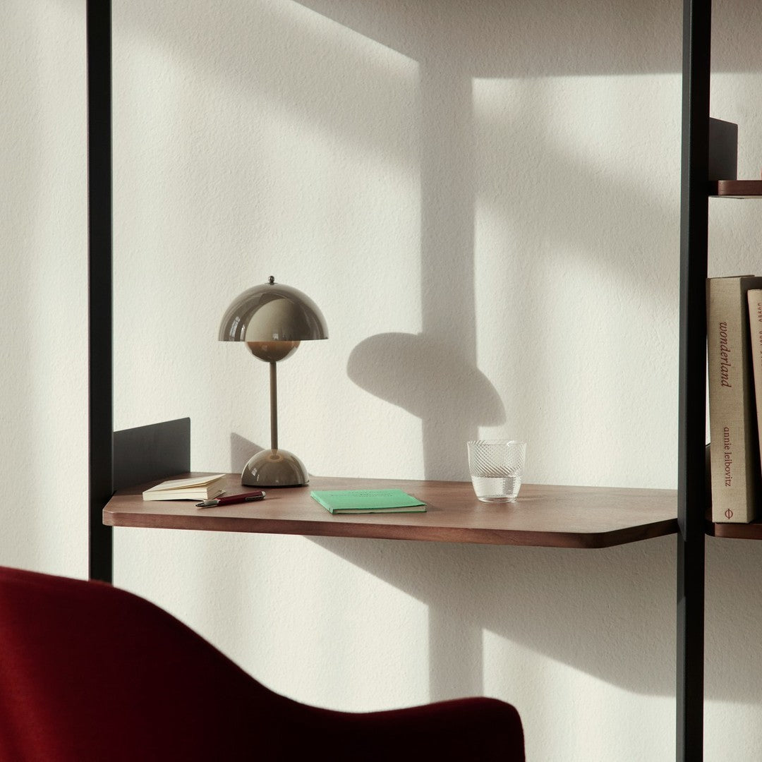 Wooden desk in warm walnut tones, beige lamp, green notebook, and clear glass, accented by soft shadows.