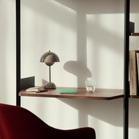 Wooden desk in warm walnut tones, beige lamp, green notebook, and clear glass, accented by soft shadows.