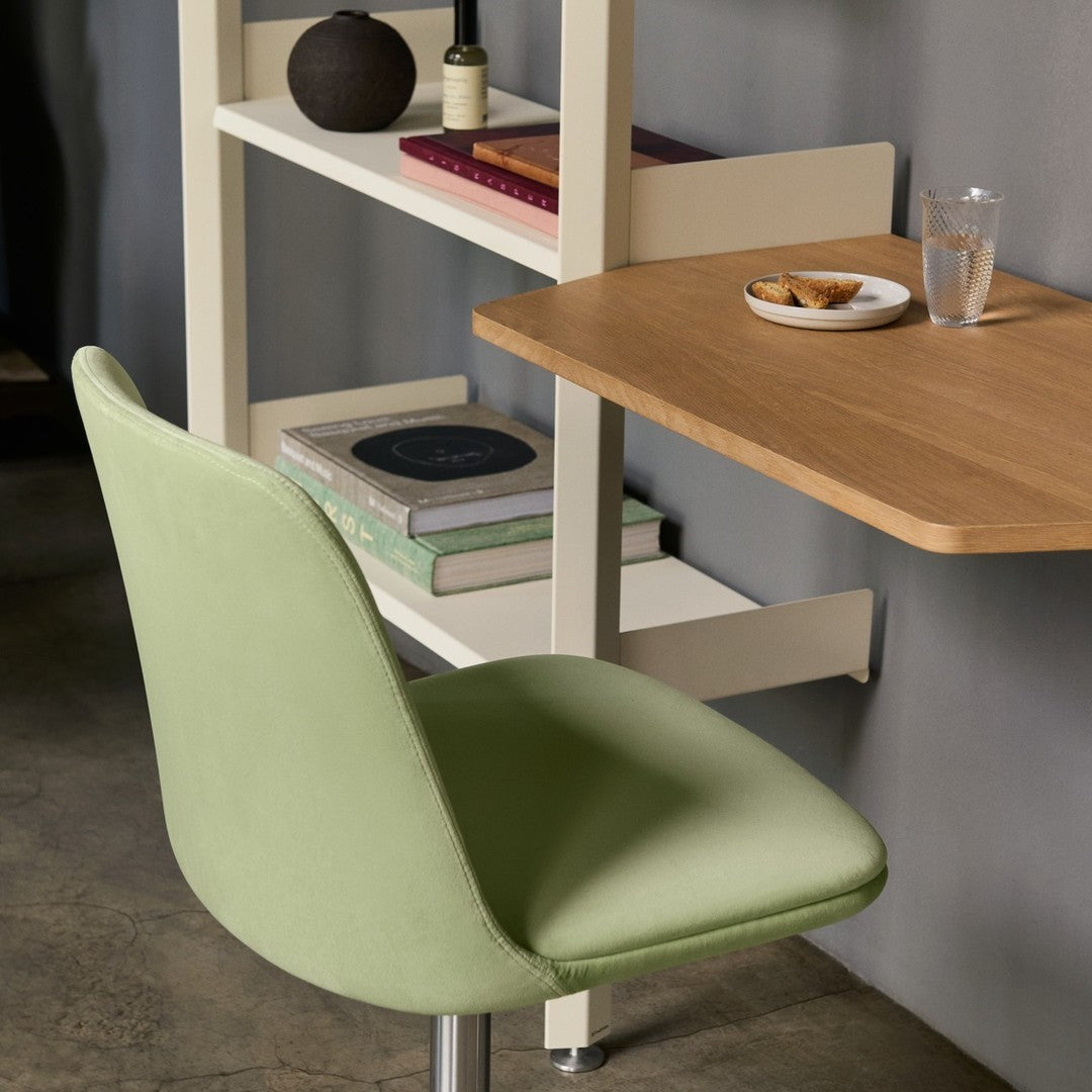 Green upholstered chair with a smooth texture, set against a gray wall, featuring natural wood tones and minimalist patterns.