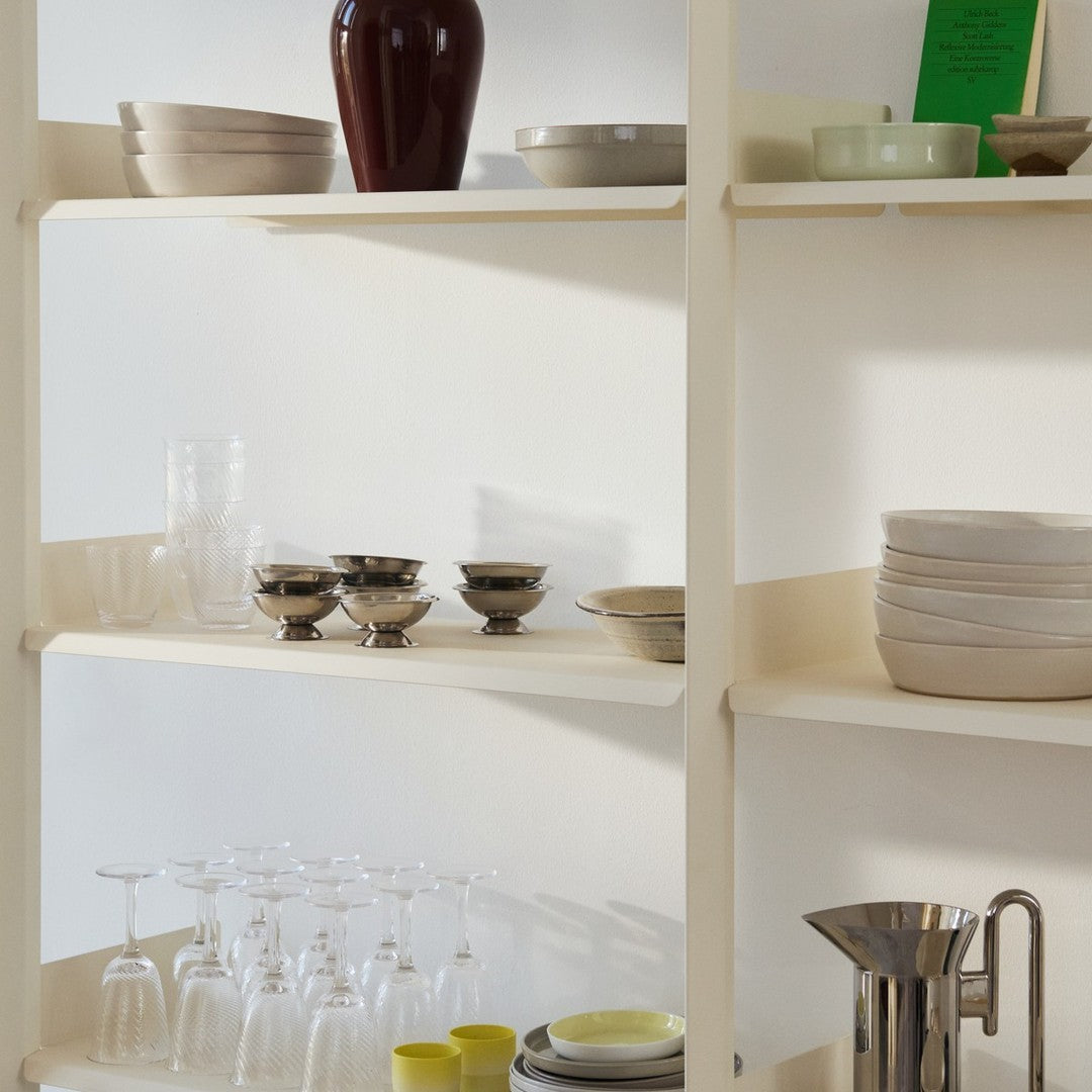 Neutral-toned tableware on shelves, featuring cream, gray, silver, and a pop of vibrant yellow for a modern aesthetic.