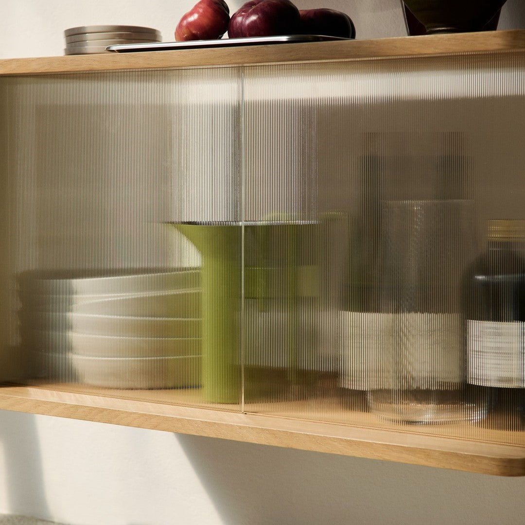 Glass cabinet showcasing green accents, textured patterns, and white dishware against a warm wood backdrop.