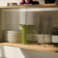 Glass cabinet showcasing green accents, textured patterns, and white dishware against a warm wood backdrop.