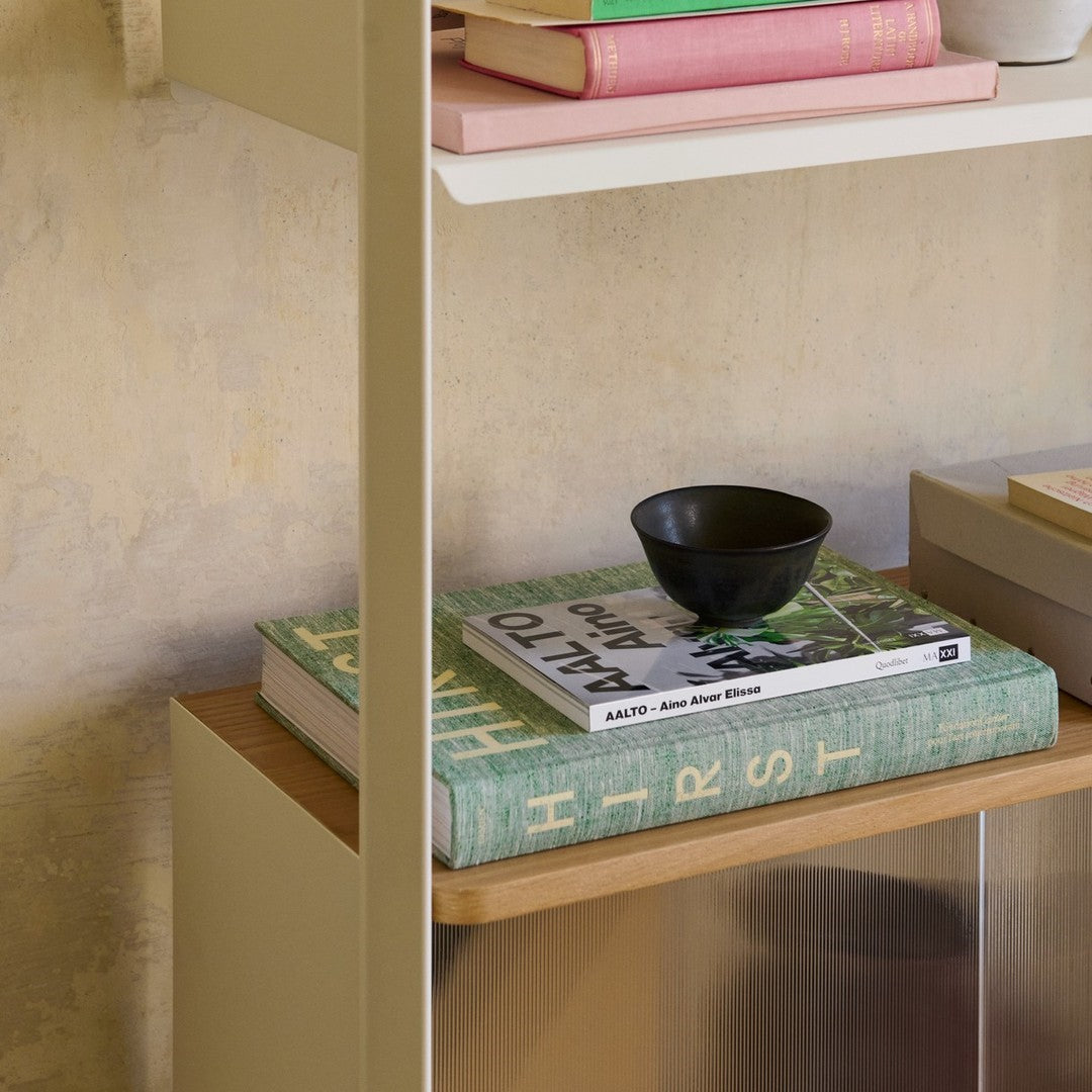 Green, pink, and black items on a stylish shelf with patterned book covers and natural wood accents.