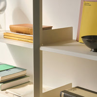 Light wood and beige shelves display stacked books in earthy tones, featuring yellow, pink, and green covers with striped patterns.
