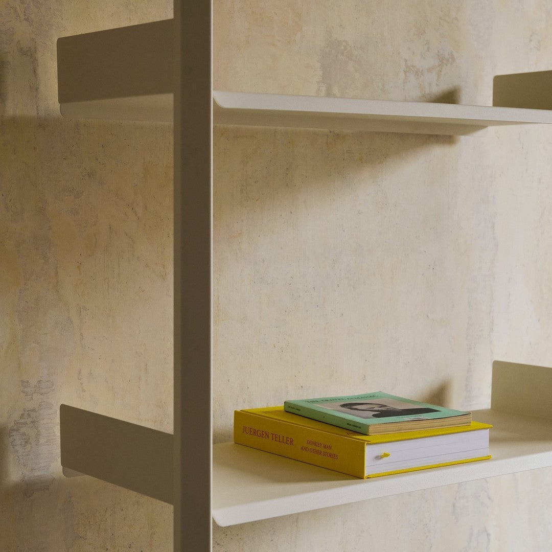 Light beige wall with subtle texture; white shelves holding green and yellow books create a modern, minimalistic look.