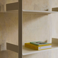 Light beige wall with subtle texture; white shelves holding green and yellow books create a modern, minimalistic look.
