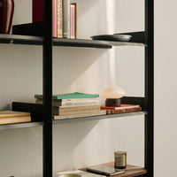 Black shelving unit with colorful books, green and orange accents, and a soft-lit lamp against a neutral background.