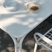 White dining table with clean lines, paired with a patterned chair and soft green dish, creating a minimalist aesthetic.