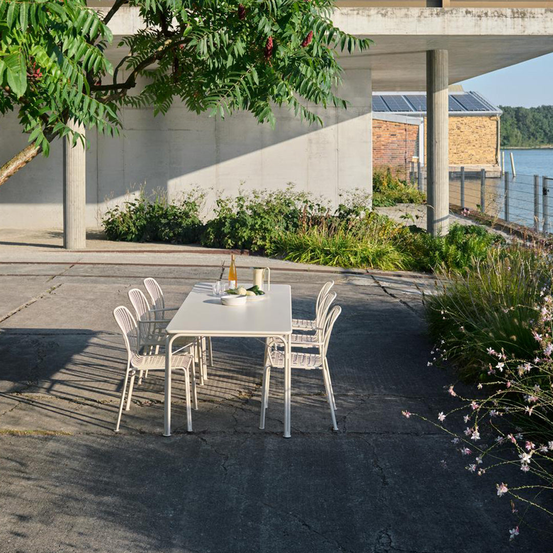 "White outdoor dining set with sleek lines, surrounded by green foliage and natural textures."