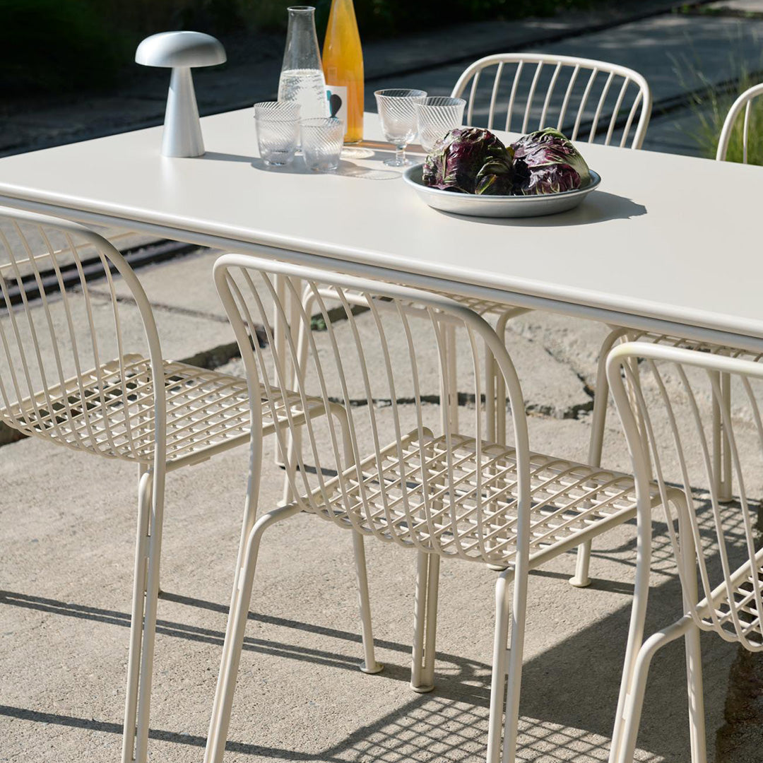 "Light beige outdoor dining table with woven cream chairs, featuring a minimalist design and natural textures."