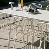 "Light beige outdoor dining table with woven cream chairs, featuring a minimalist design and natural textures."