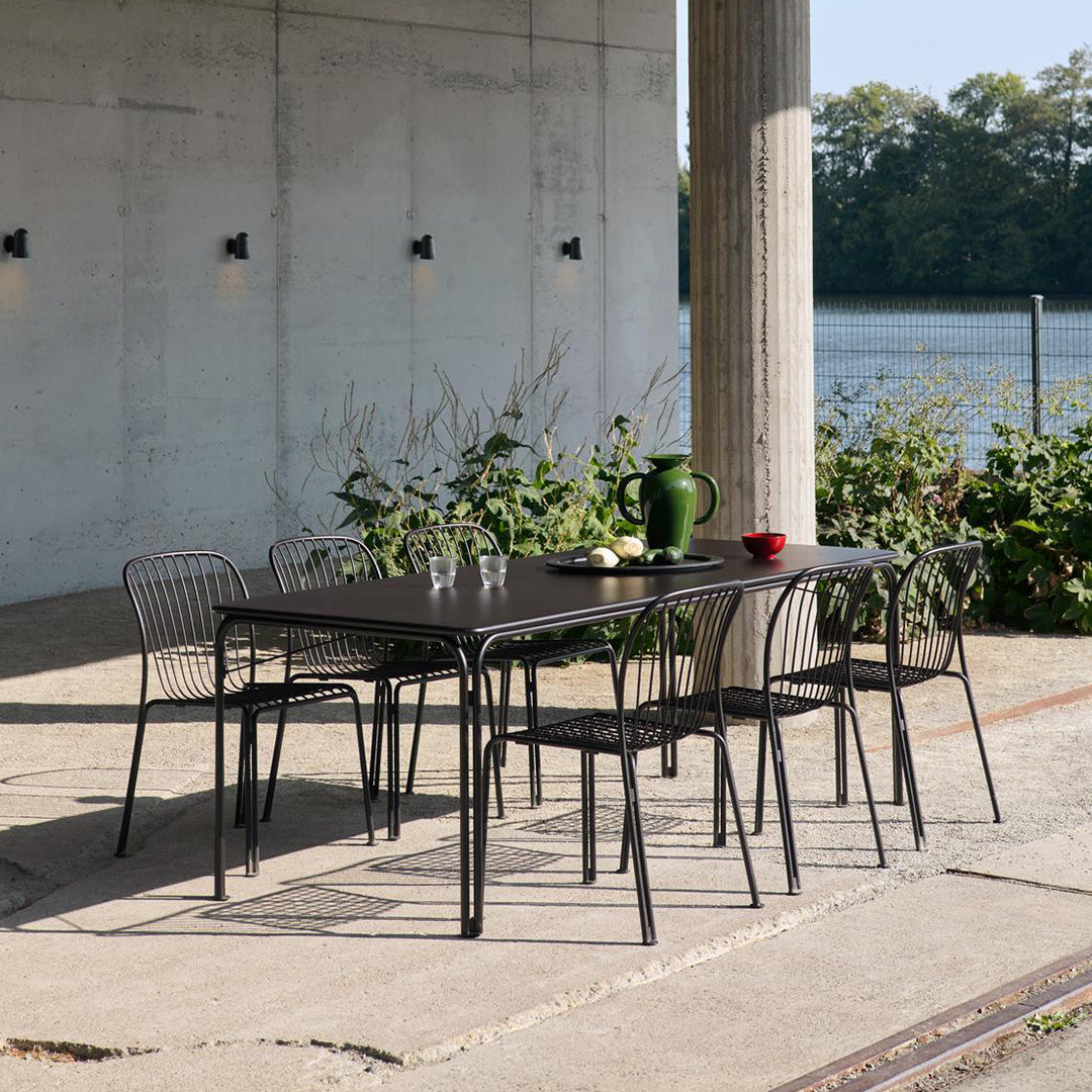 Black metal dining table with minimalist lines, paired with matching wire chairs in a natural outdoor setting.