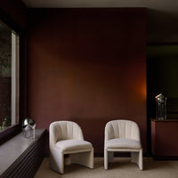 "White textured chairs against a rich burgundy wall and warm brown accents, creating a cozy, modern aesthetic."