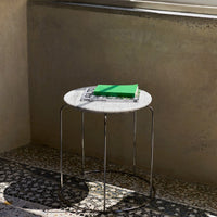 Round marble side table with a white top and silver legs, featuring a green book and a textured patterned floor.
