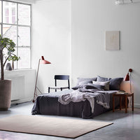 "Neutral-toned bedroom featuring gray bedding, a muted rug, and earthy green plant accents."