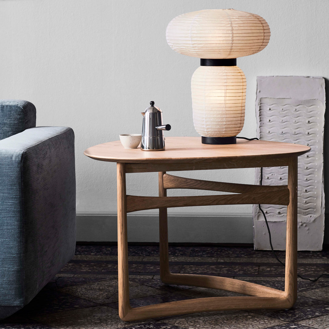 Light wood coffee table with an oval top and geometric legs, paired with a soft white lamp on a textured rug.