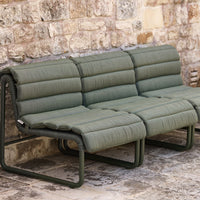 Olive green padded sofa with a sleek fabric design and modern metal frame against a rustic stone wall.