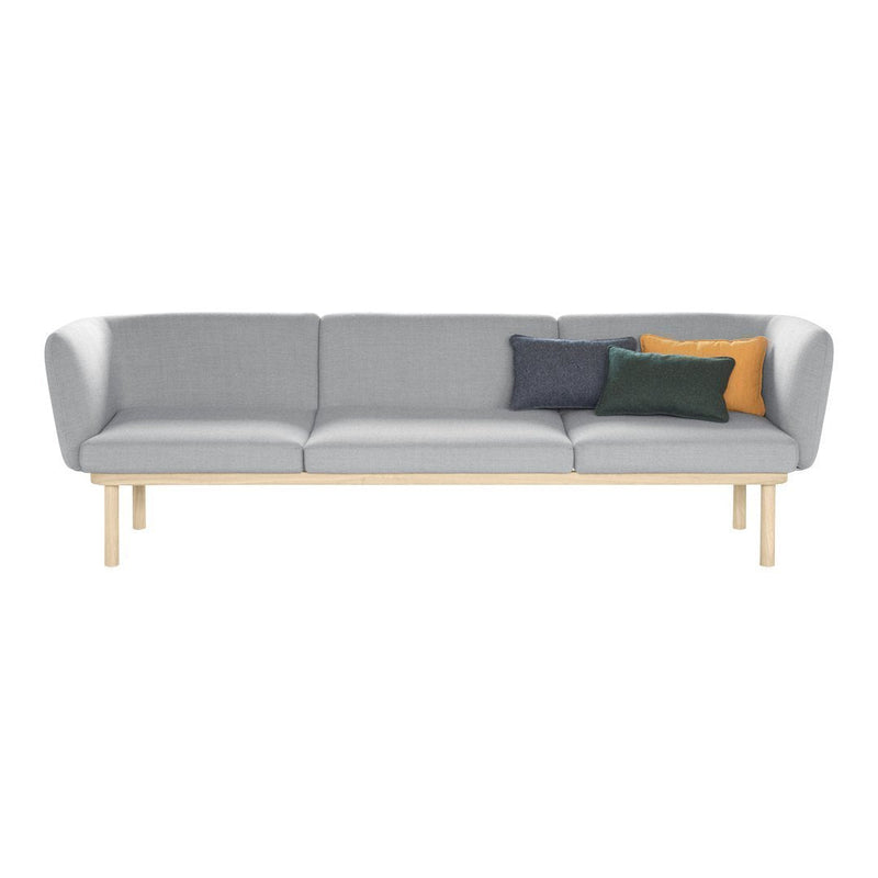 Light gray sofa with three accent pillows in green, navy, and mustard against a light wood frame.