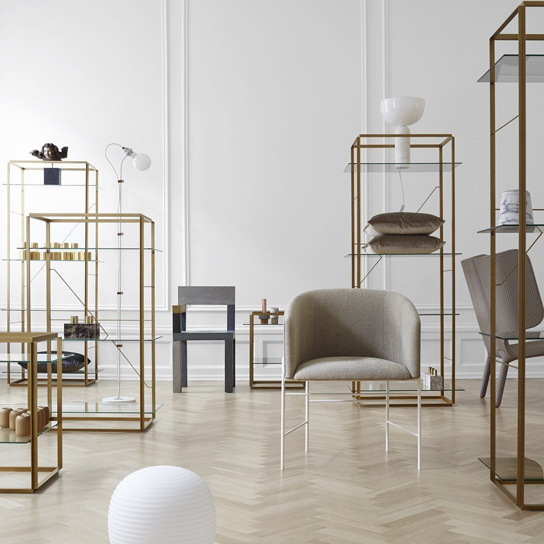 "Modern display shelves with gold frames, beige chair, and minimalist decor against a light wood herringbone floor."