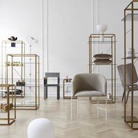 "Modern display shelves with gold frames, beige chair, and minimalist decor against a light wood herringbone floor."