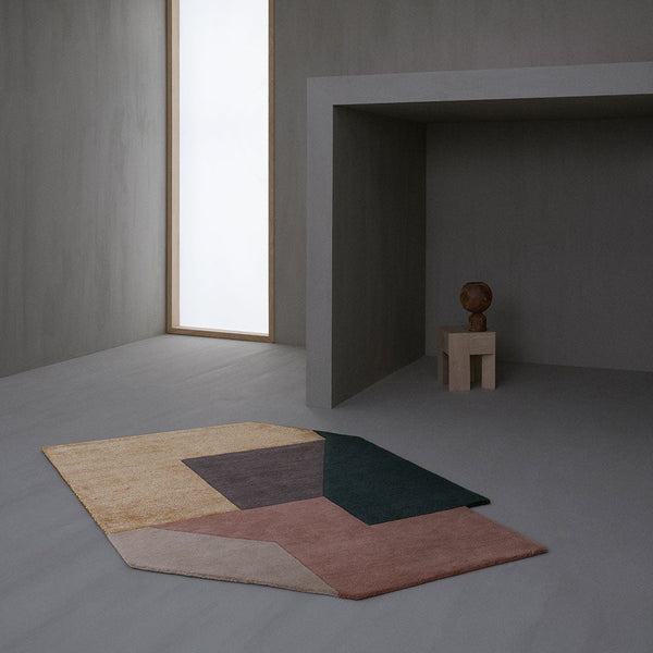 Geometric area rug featuring muted tones of pink, mustard, deep green, and brown on a textured background.