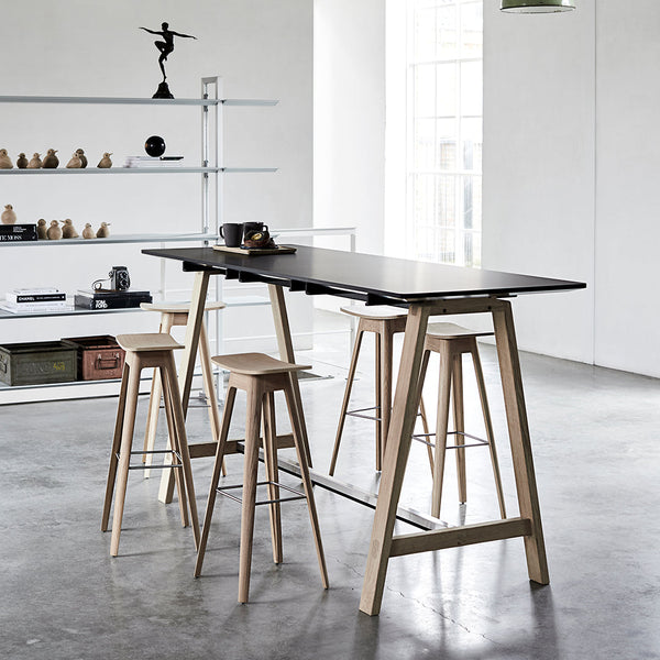 Modern black tabletop with natural wood bar stools on a concrete floor, featuring sleek, minimalist design.