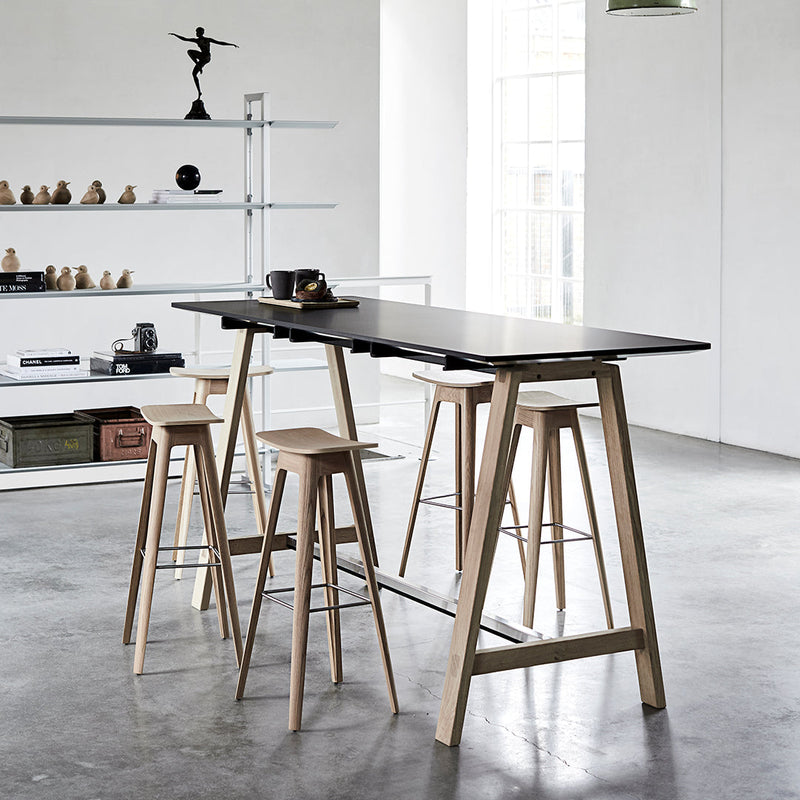 Modern black tabletop with natural wood bar stools on a concrete floor, featuring sleek, minimalist design.