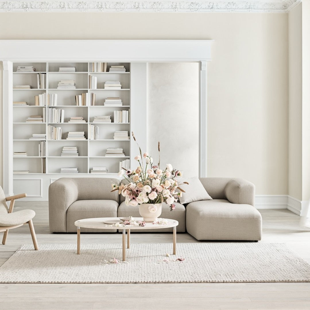 Beige curved sofa in a minimalist room with a neutral rug and soft pastel floral arrangement. Elegant and contemporary design.