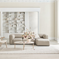 Beige curved sofa in a minimalist room with a neutral rug and soft pastel floral arrangement. Elegant and contemporary design.