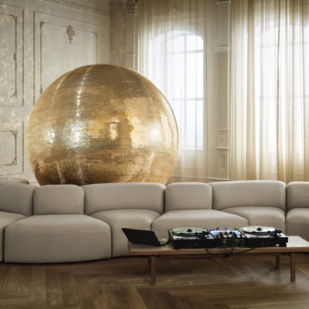 Gold disco ball shines in a neutral-toned living room with soft beige couch and warm wooden floor patterns.