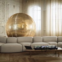 Gold disco ball shines in a neutral-toned living room with soft beige couch and warm wooden floor patterns.