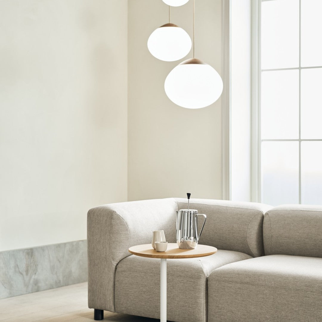 Light gray sectional sofa with soft, textured fabric, complemented by a minimalist wooden side table and bright round pendant lights.