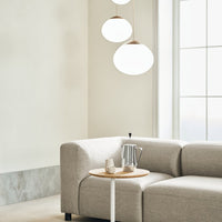 Light gray sectional sofa with soft, textured fabric, complemented by a minimalist wooden side table and bright round pendant lights.