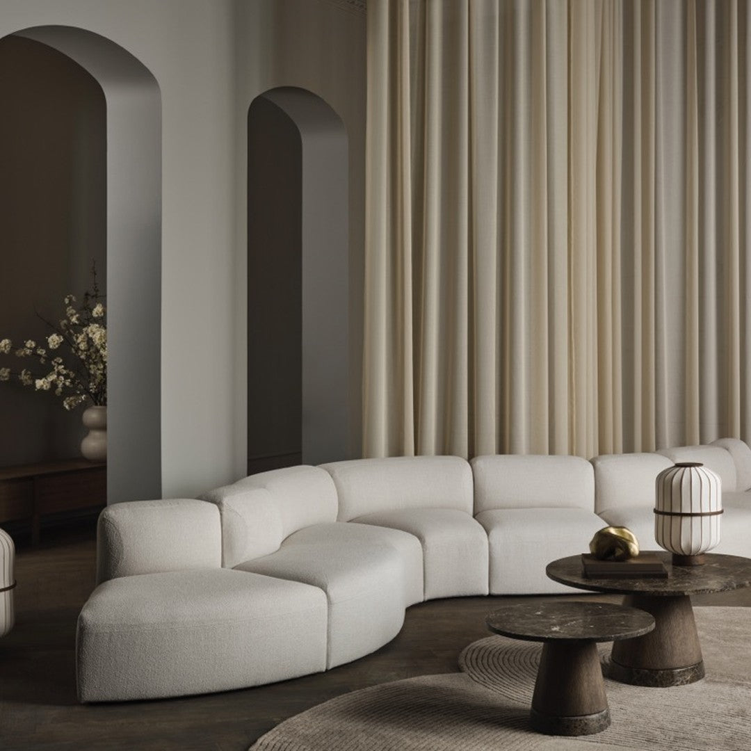 Curved cream sofa against beige walls and soft drapes, featuring dark wood tables and natural textures.