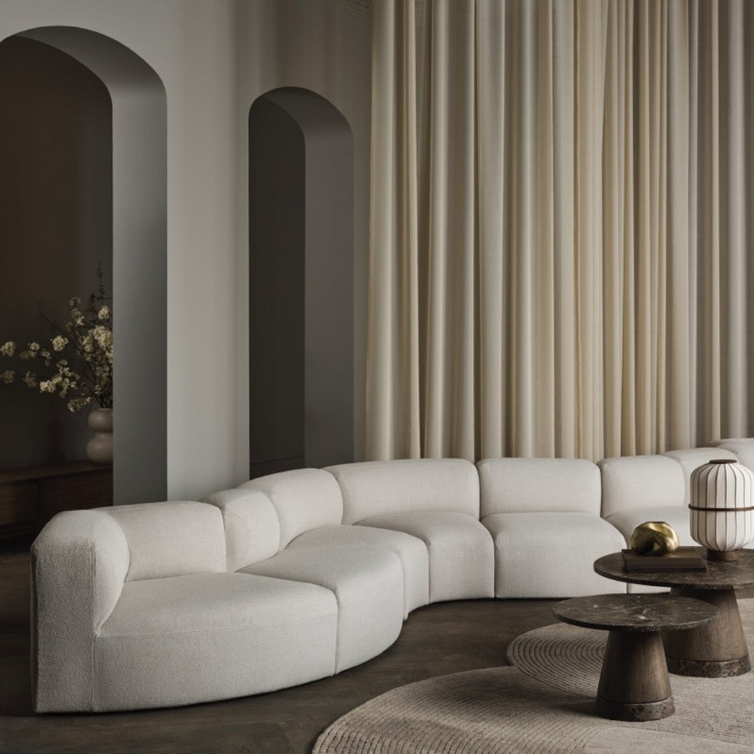 Curved white sofa with soft textures against beige curtains and muted gray walls, creating a serene, modern aesthetic.