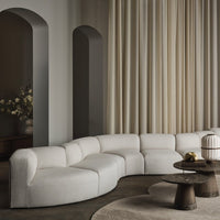 Curved white sofa with soft textures against beige curtains and muted gray walls, creating a serene, modern aesthetic.