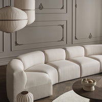 Light beige curved sofa with textured fabric, complemented by soft grey walls and patterned hanging lamps.
