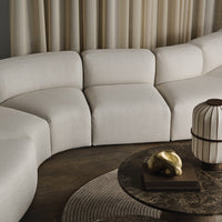 Cream-colored curved sofa with textured fabric and matching neutral tones, accented by a dark wood table and decor.