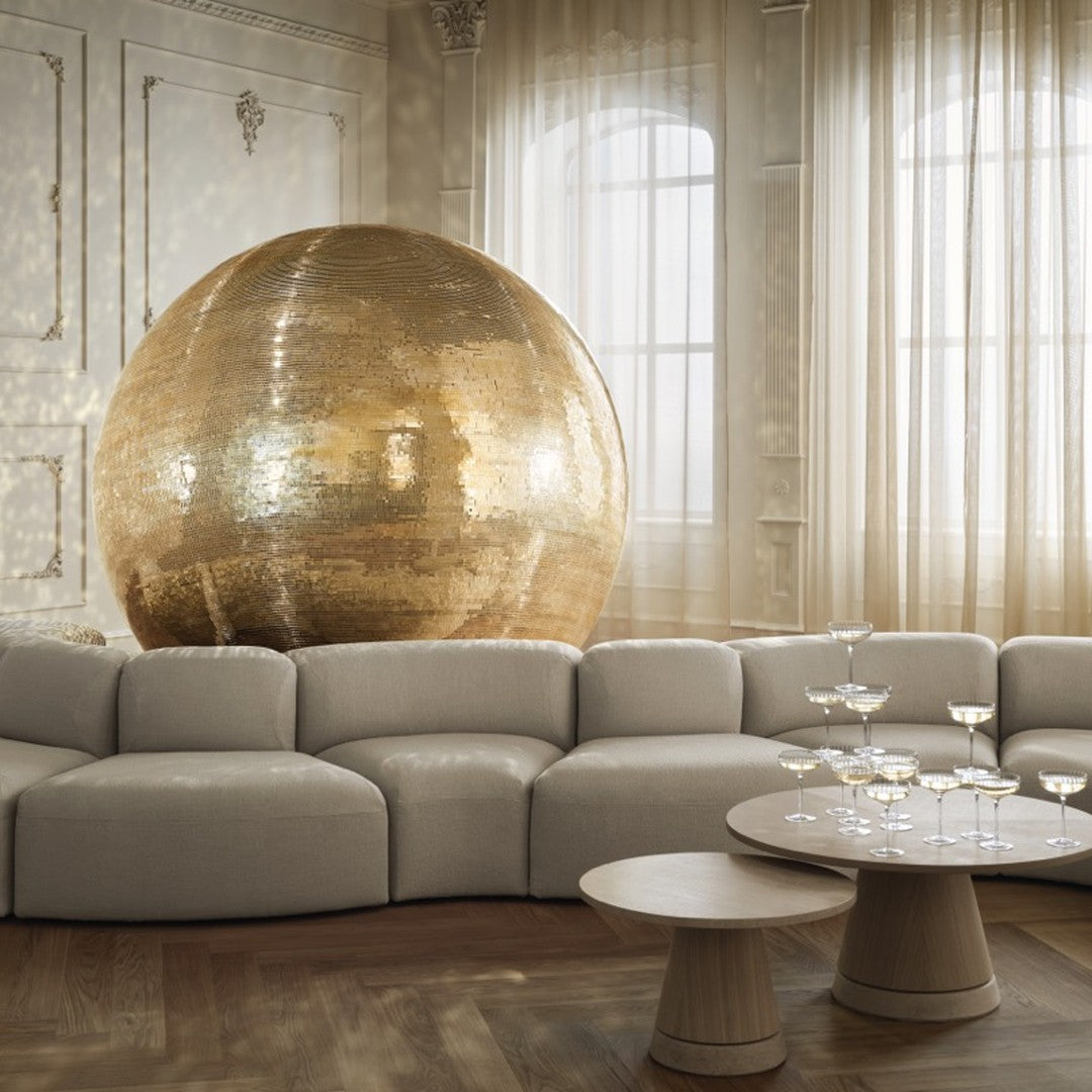 Gold sequined sphere with a soft beige sofa and natural wood table, creating a cozy, elegant living space.