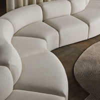 Curved beige sectional sofa with textured fabric on a dark wooden floor, complemented by a circular brown rug.